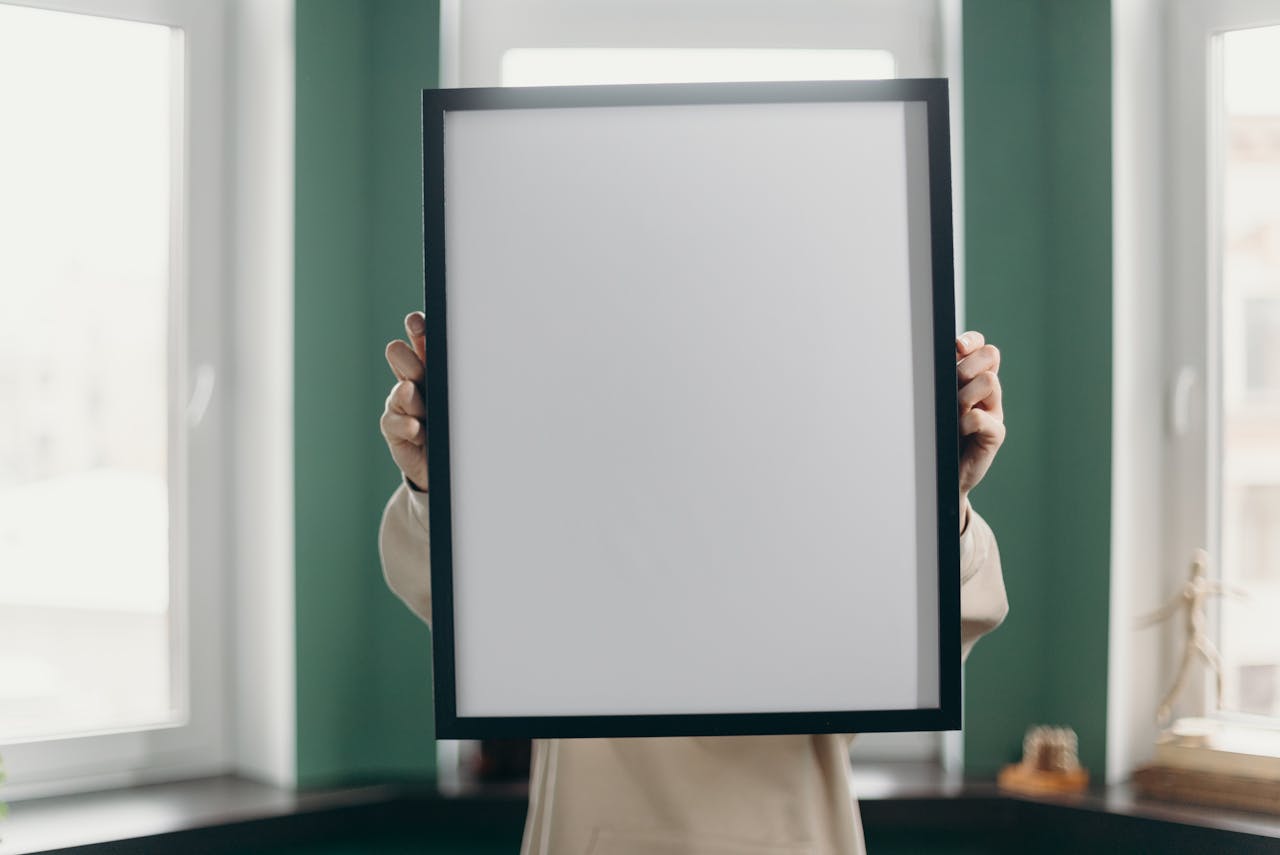 Adult holding a blank photo frame in an indoor, minimalist setting. Ideal for mockups and design.